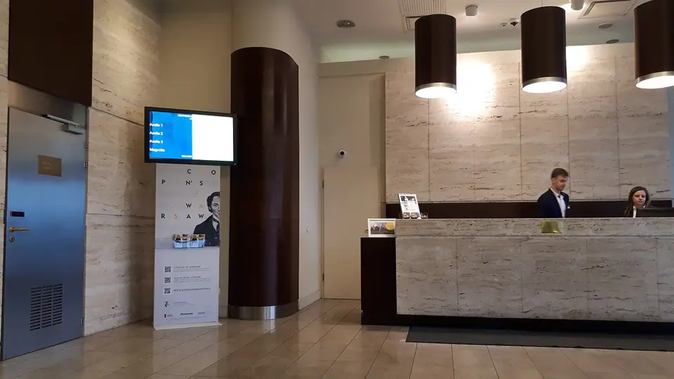 Mermer kaplı bir otel resepsiyon bankosu, sarkıt lambalar ve bilgi ekranı