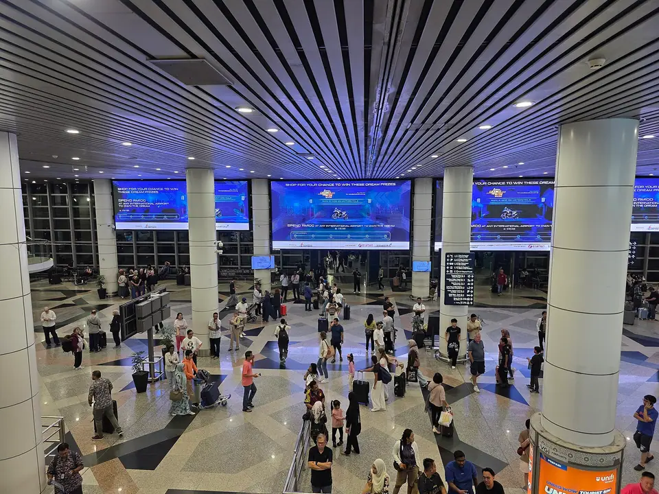 Yüksek tavanlı bir havalimanı terminalinde yolcular ve bilgi ekranları